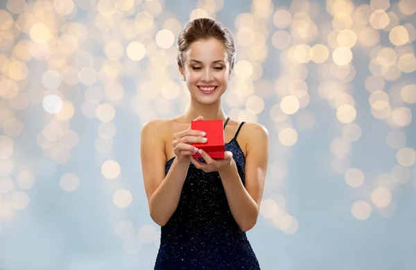Mujer sonriente sosteniendo caja de regalo roja sobre luces — Foto de Stock