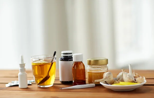 Medicamentos, termómetro, miel y taza de té sobre madera — Foto de Stock