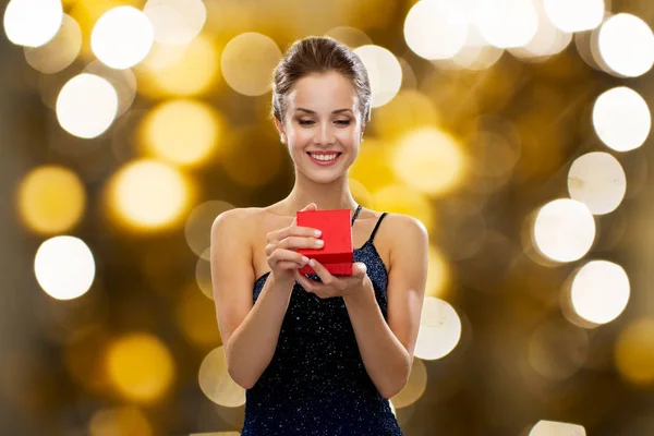Sorrindo mulher segurando caixa de presente vermelho sobre luzes — Fotografia de Stock