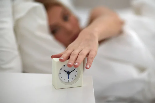 Close up of woman with alarm clock in bed at home — Stock Photo, Image