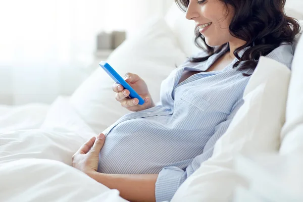 Close up van zwangere vrouw met smartphone in bed — Stockfoto