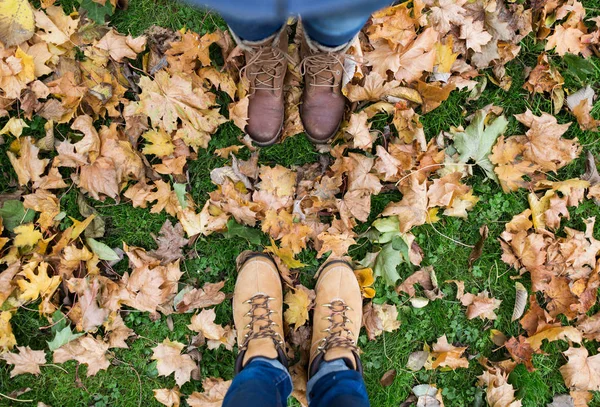 Par de pies en botas y hojas de otoño —  Fotos de Stock