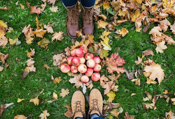 Piedi in stivali con mele e foglie autunnali — Foto Stock