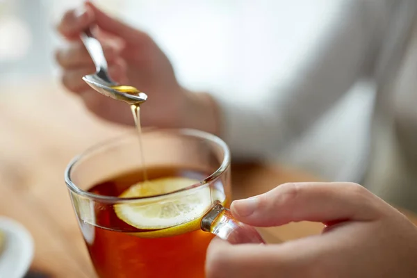 Gros plan de la femme ajoutant du miel au thé avec du citron — Photo