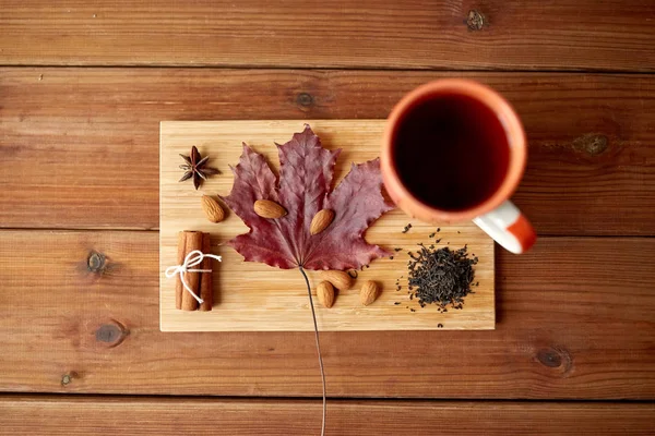 Tazza di tè, foglia d'acero e mandorla su tavola di legno — Foto Stock