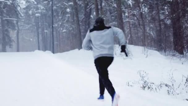 Hombre corriendo sobre nieve cubierto invierno camino en bosque — Vídeo de stock