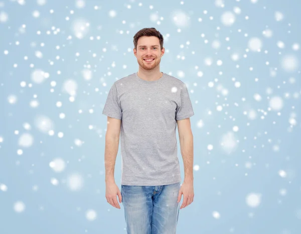 Jovem sorridente em t-shirt e jeans sobre a neve — Fotografia de Stock