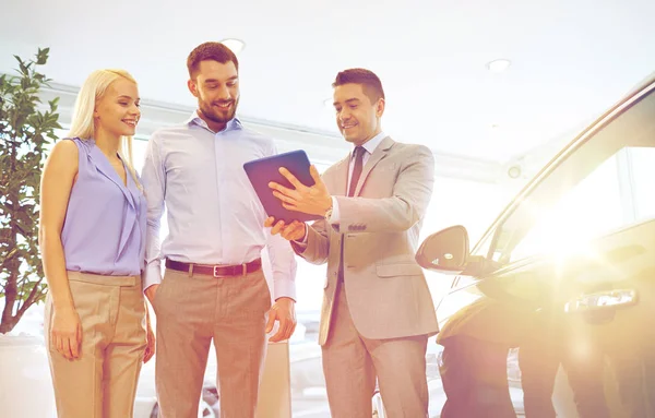 Glückliches Paar mit Autohändler in Auto-Show oder Salon — Stockfoto