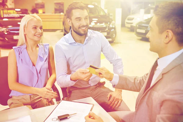 Glückliches Paar mit Autohändler in Auto-Show oder Salon — Stockfoto