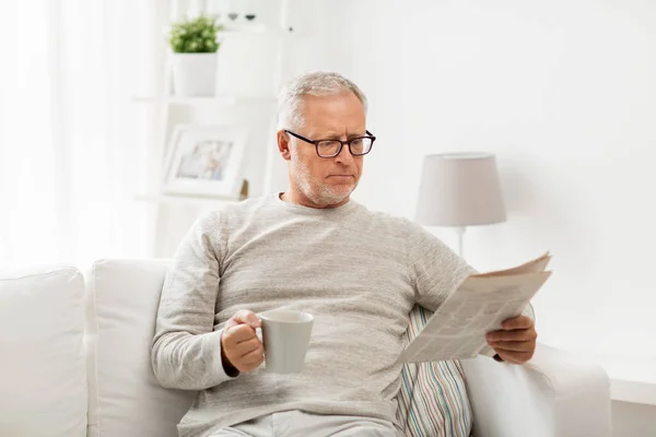 Hombre mayor en gafas leyendo el periódico en casa — Foto de Stock