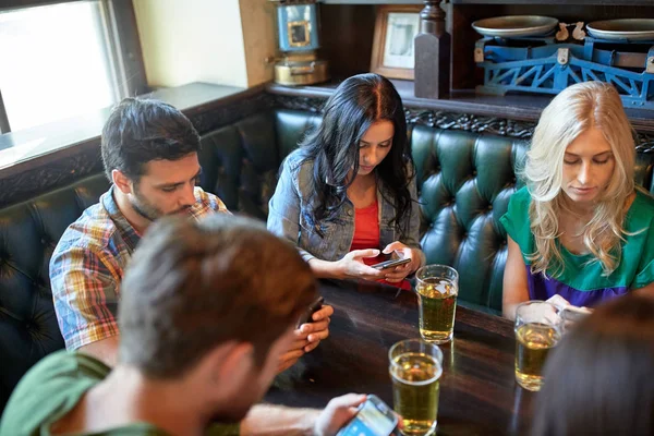 Друзья со смартфонами и пивом в баре или пабе — стоковое фото
