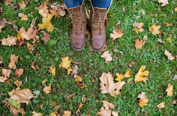 Pés femininos em botas e folhas de outono na grama — Fotografia de Stock