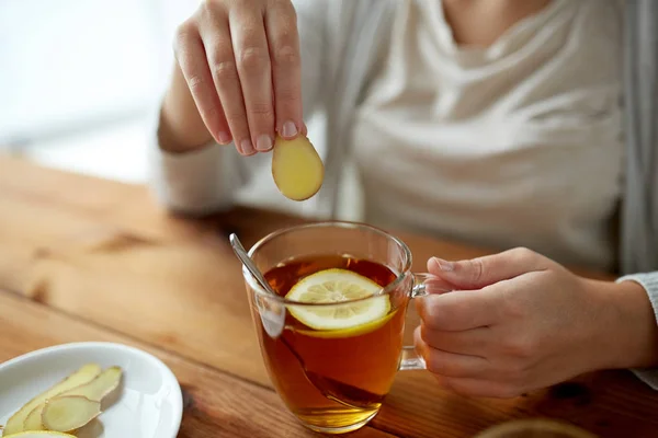 Nahaufnahme einer Frau, die Ingwer zum Tee mit Zitrone hinzufügt — Stockfoto