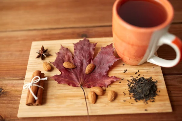 Taza de té, hoja de arce y almendra sobre tabla de madera — Foto de Stock