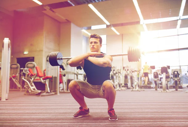 Joven hombre flexionando los músculos con barra en el gimnasio —  Fotos de Stock