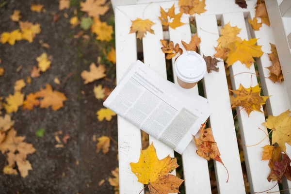 Noviny a káva pohár na lavičce na podzim park — Stock fotografie
