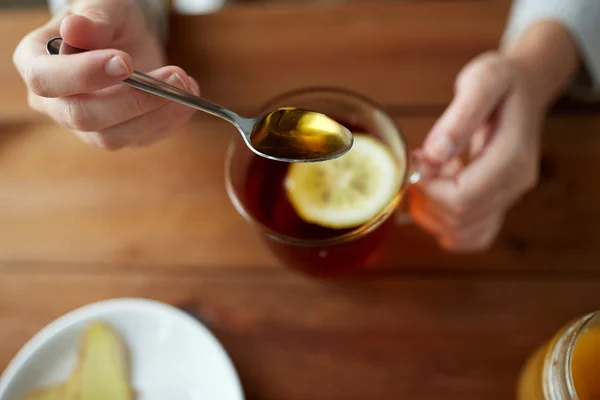 Primo piano di donna che aggiunge miele al tè con limone — Foto Stock