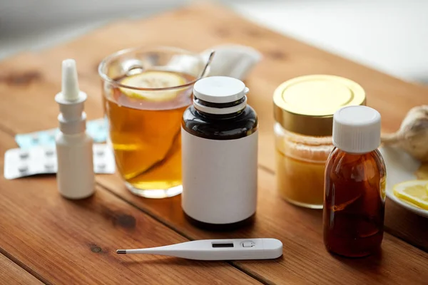 Medicamentos, termómetro, miel y taza de té sobre madera — Foto de Stock