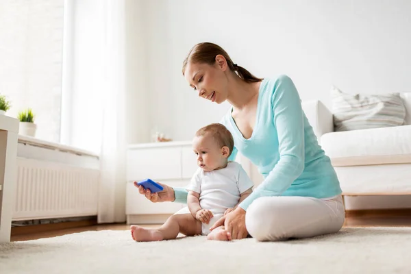 Mãe feliz mostrando smartphone para bebê em casa — Fotografia de Stock