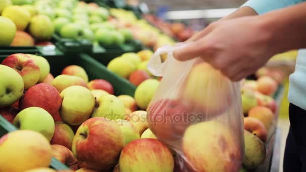 Женщина кладет яблоко в сумку в продуктовом магазине — стоковое видео