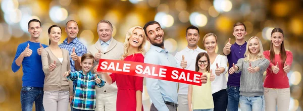 Persone felici con segno di vendita mostrando pollici in su — Foto Stock