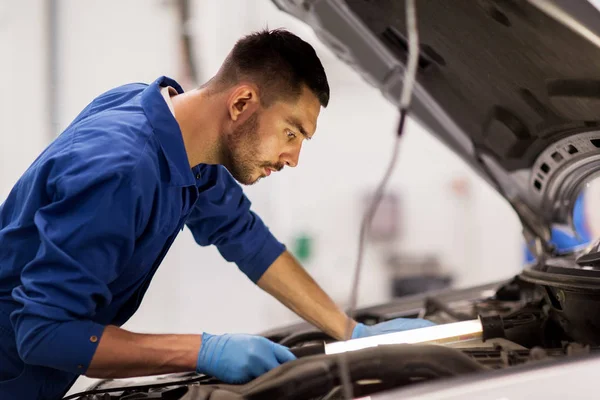 Mechanic man with lamp repairing car at workshop — Stock Photo, Image