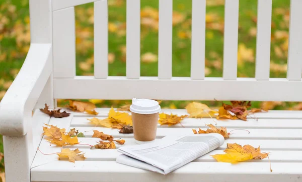 Periódico y taza de café en el banco en el parque de otoño — Foto de Stock