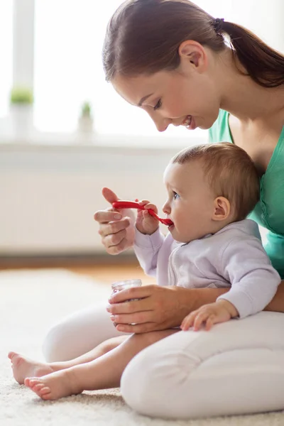 Madre feliz con cuchara alimentando al bebé en casa — Foto de Stock