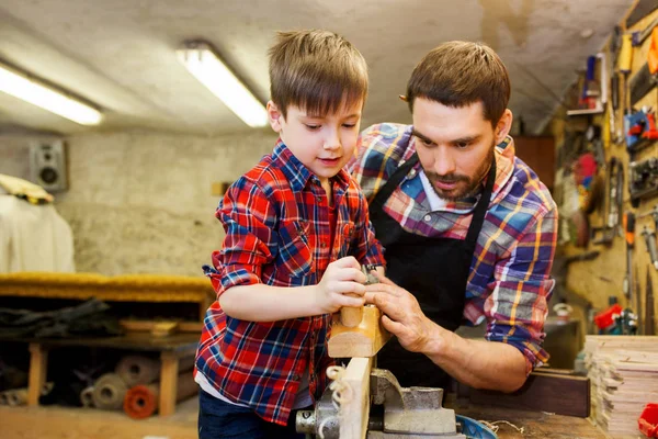 Father and son with plane shaving wood at workshop — Stock Photo, Image