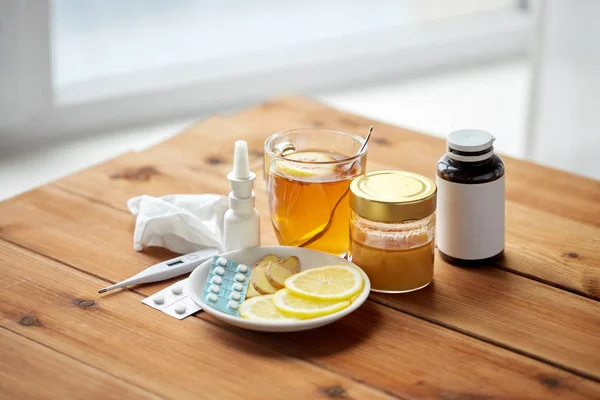 Medicamentos, termómetro, miel y taza de té sobre madera — Foto de Stock