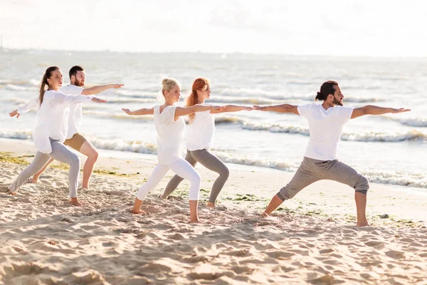 People making yoga in warrior pose on beach — Stock Photo, Image