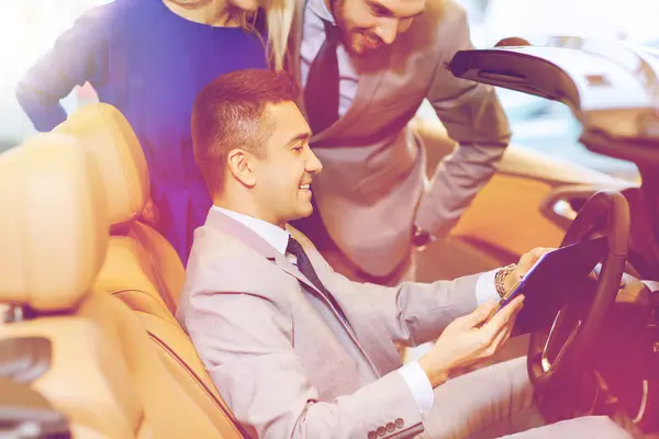 Casal feliz com revendedor de carro em auto show ou salão — Fotografia de Stock