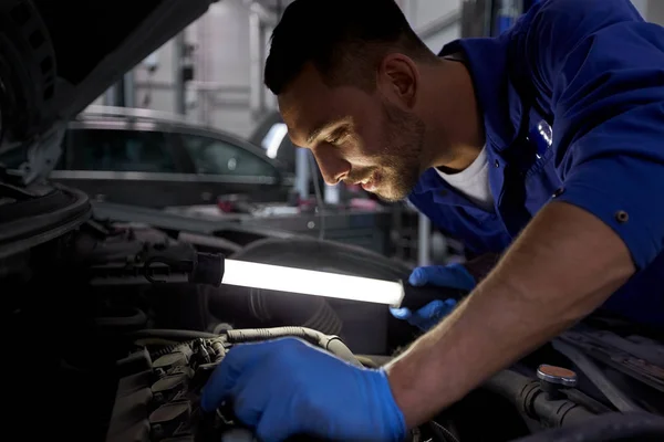 Механічний чоловік з лампою ремонтує автомобіль на майстерні — стокове фото