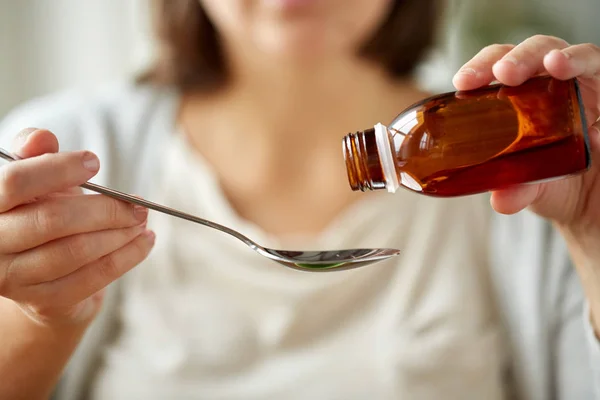 Женщина наливает лекарства из бутылки в ложку — стоковое фото