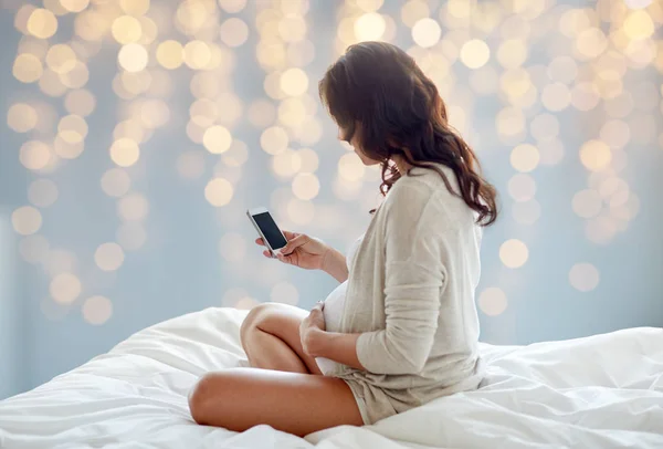 Pregnant woman with smartphone in bed — Stock Photo, Image