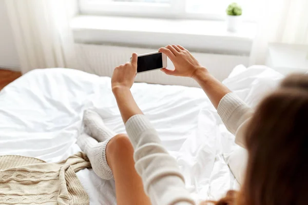 Woman photographing with smartphone in bet at home — Stock Photo, Image