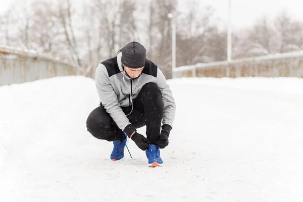 Hombre con auriculares atando zapato deportivo en invierno — Foto de Stock