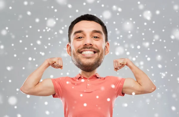 Улыбающийся мужчина показывает бицепсы на фоне снега — стоковое фото