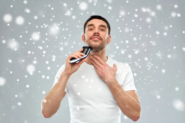 Улыбающийся мужчина бреет бороду с триммером над снегом — стоковое фото