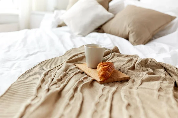 Taza de café y croissant a cuadros en la cama en casa —  Fotos de Stock