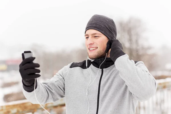 Šťastný muž s sluchátka a smartphone v zimě — Stock fotografie
