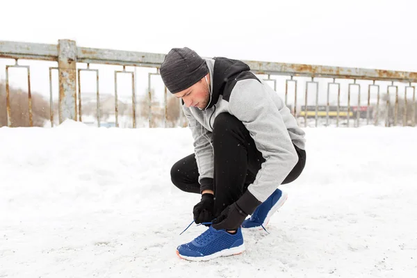 Człowiek z słuchawki, wiązanie butów sportowych zimą — Zdjęcie stockowe