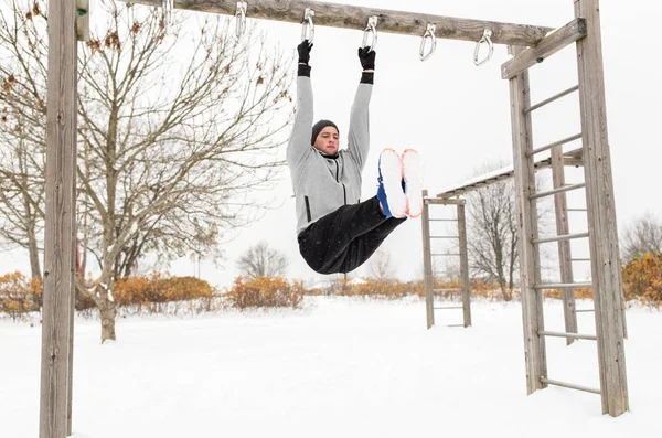 young man exercising on horizontal bar in winter