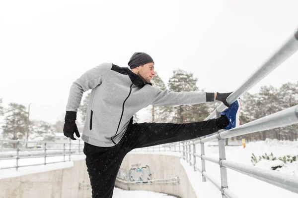 Sportovní muž strečink nohou na plot v zimě — Stock fotografie