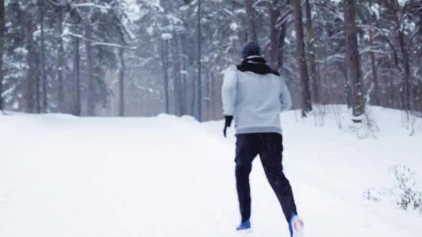 Homem correndo na neve coberto estrada de inverno na floresta — Vídeo de Stock