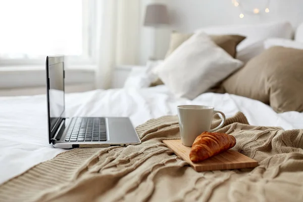 Portátil, café y croissant en la cama en casa acogedora —  Fotos de Stock