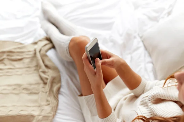 Gelukkig jonge vrouw met smartphone in bed thuis — Stockfoto