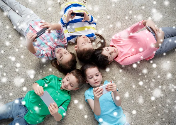 Niños felices con teléfonos inteligentes tumbados en el suelo — Foto de Stock