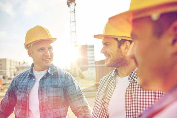 Группа улыбающихся строителей в касках на открытом воздухе — стоковое фото