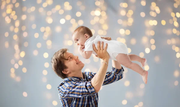 Feliz jovem pai brincando com bebê sobre luzes — Fotografia de Stock